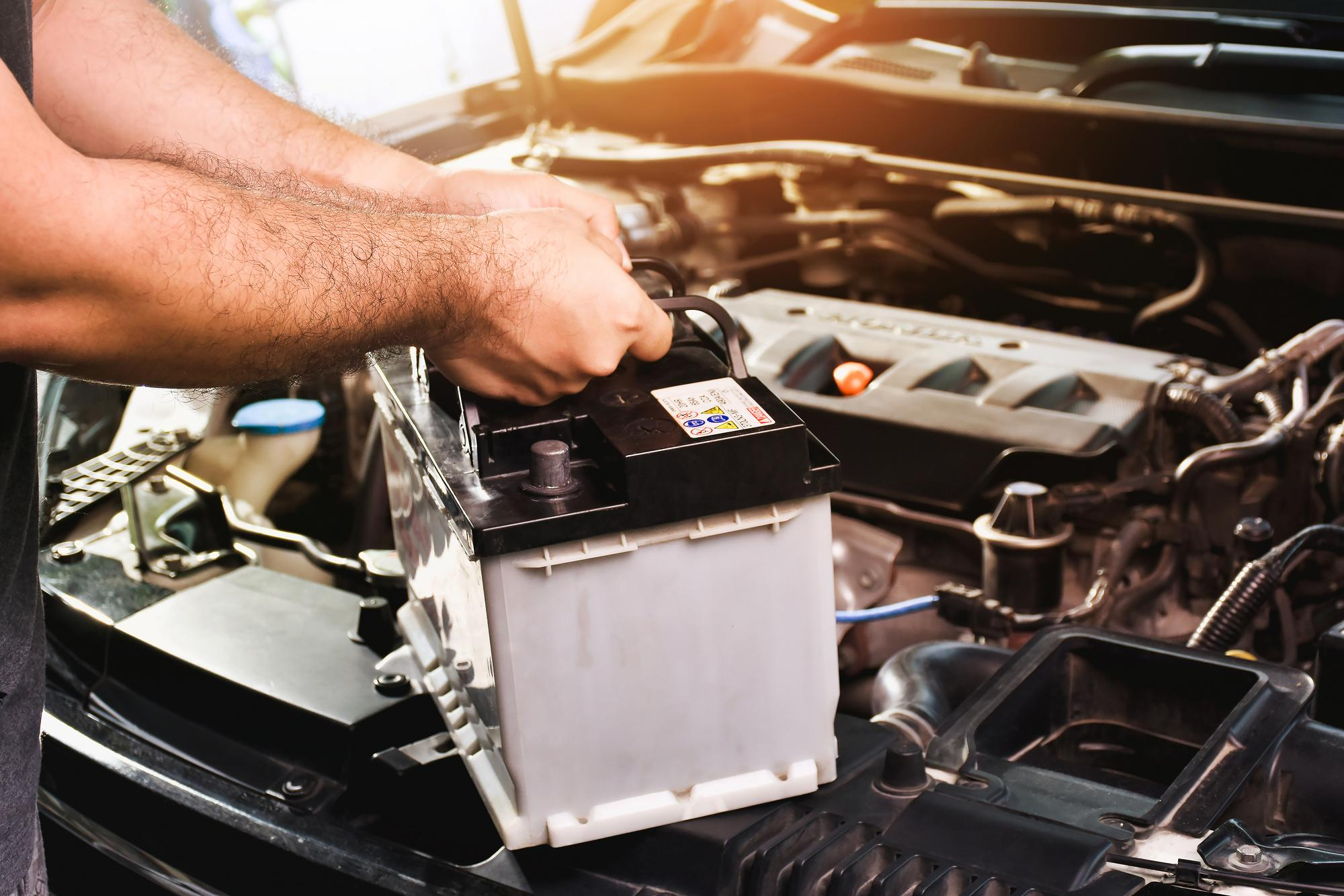 Mechanic lifting a car battery into an engine bay