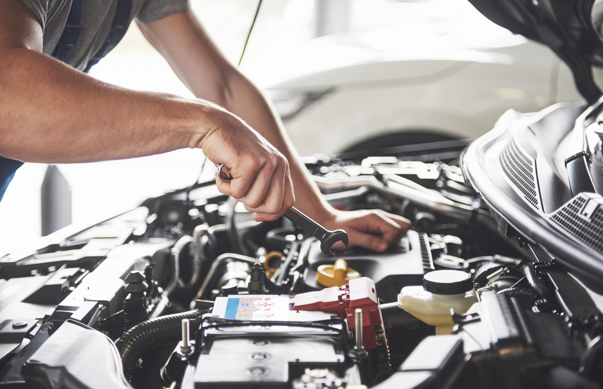 Technician tightening an engine component under a car hood